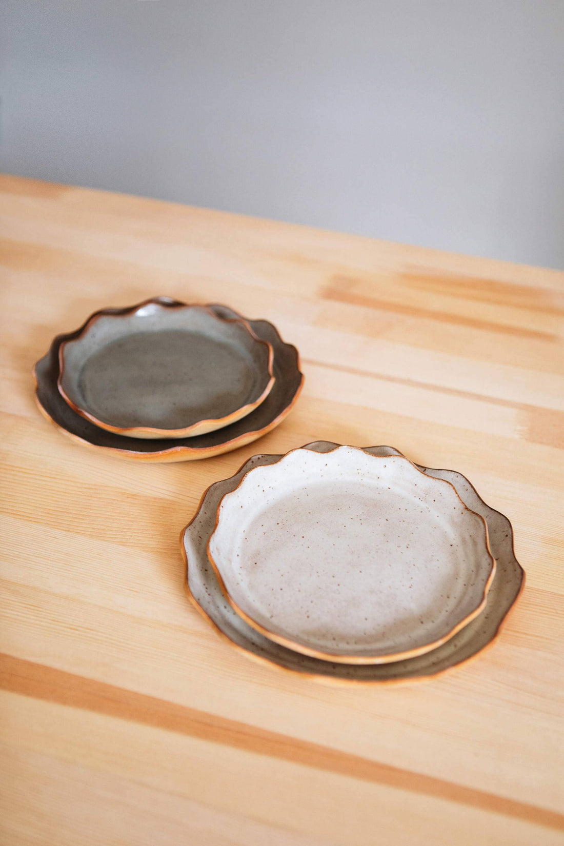 Stoneware plates, two stacked pairs with scalloped edges. Front: speckled cream interior. Back: dark gray-green interior.…