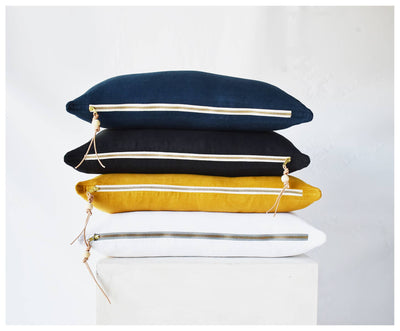 
                    
                      Blue Washed Linen throw pillow stacked atop black, yellow, and white pillows, showing brass zipper and leather pull detail.
                    
                  