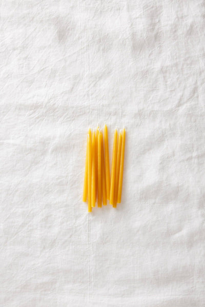 
                    
                      Beeswax Birthday Candles, a loose cluster of yellow pure beeswax candles arranged on a white linen flat lay, top-down view.
                    
                  
