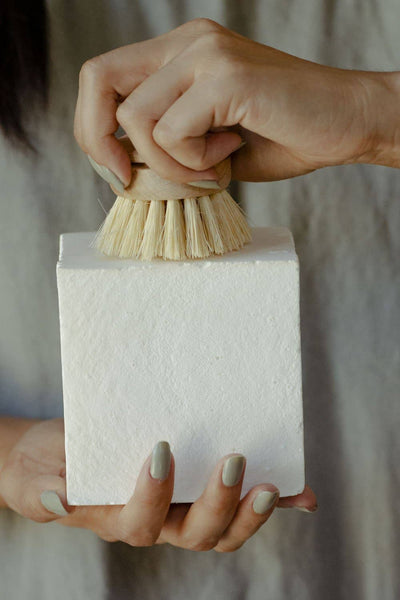
                    
                      Dish Block Solid Dish Soap, white rectangular block held by a hand, another hand scrubbing its textured surface with a small…
                    
                  