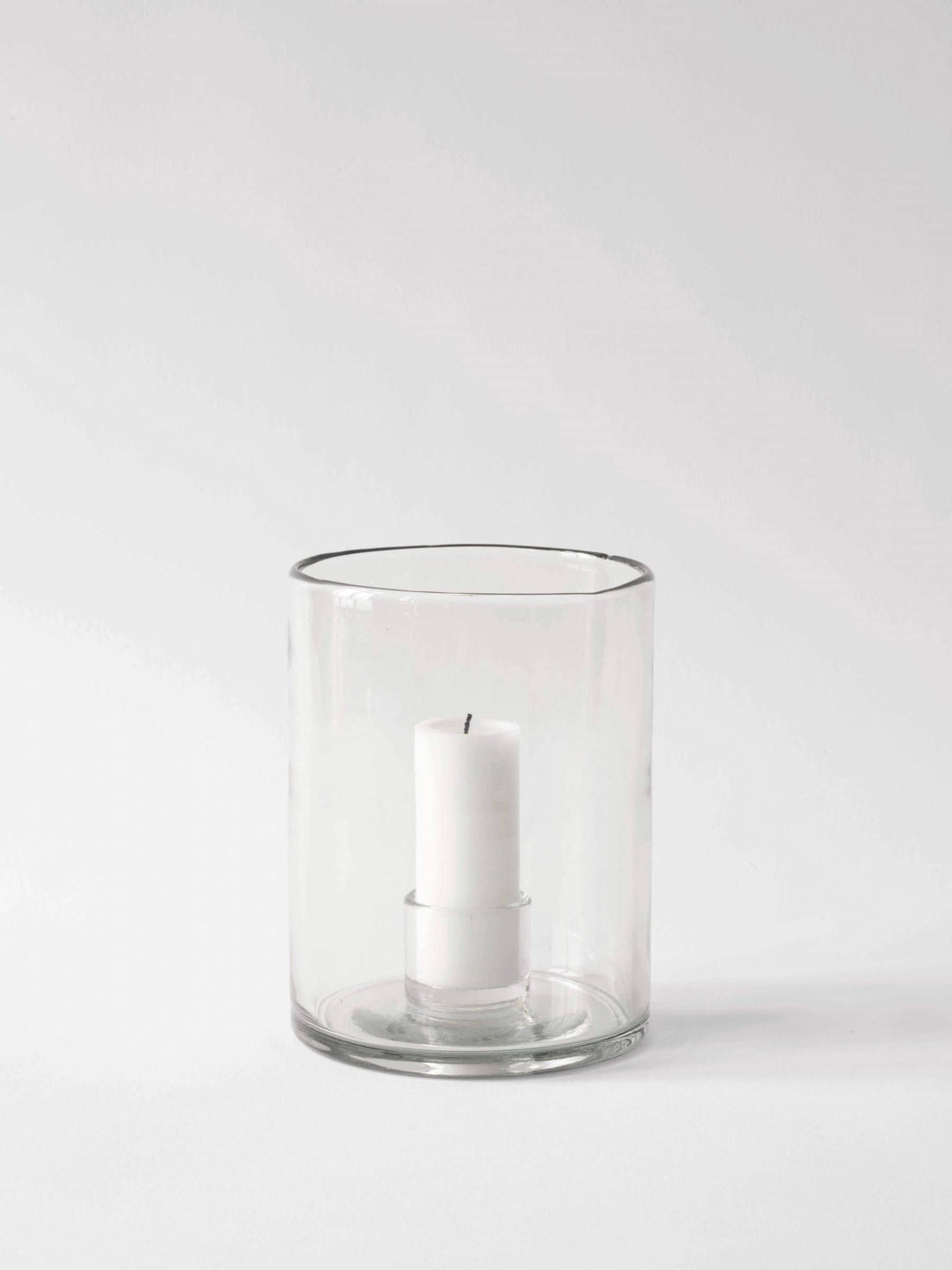 Luna candle holder, medium clear recycled glass, with white pillar candle inside, front view on white.