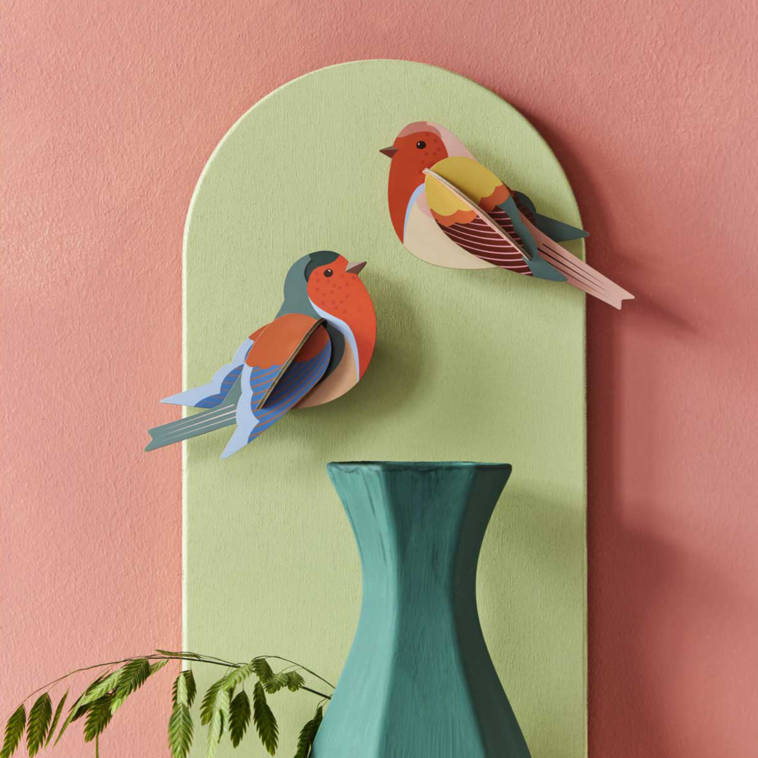 Robins 3D build kit, two colorful assembled cardboard birds in red, blue, yellow, displayed on a green arched panel.