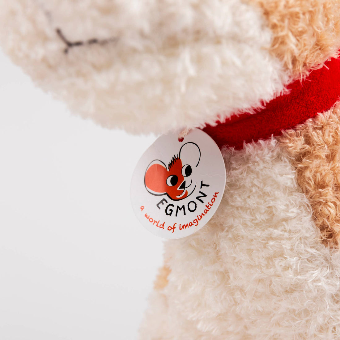 Plush Eliot Stuffed Dog: close-up of Egmont brand tag on red fabric collar, showing soft cream and tan polyester plush.