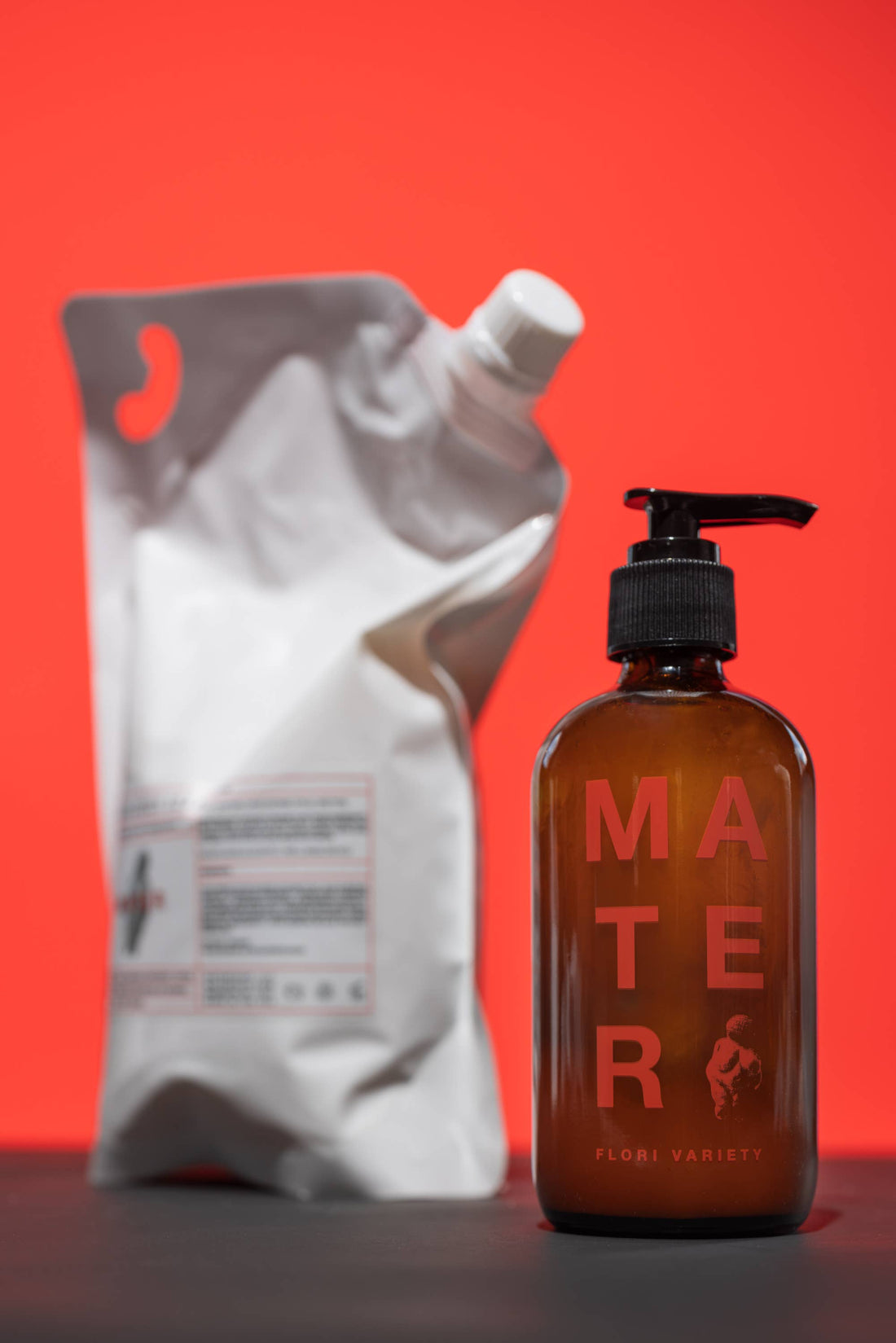 Mater Flori liquid hand soap in brown glass bottle with red Mater text and black pump, next to blurred white refill pouch.