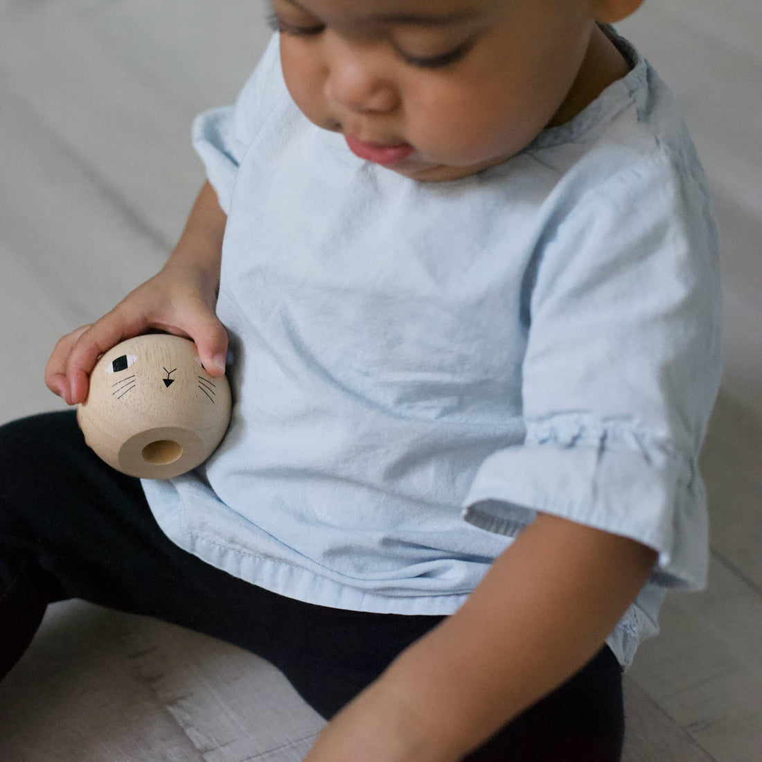 Wooden Ring Stacker Cat head piece, natural rubberwood with black facial details, held in child's hand for scale.