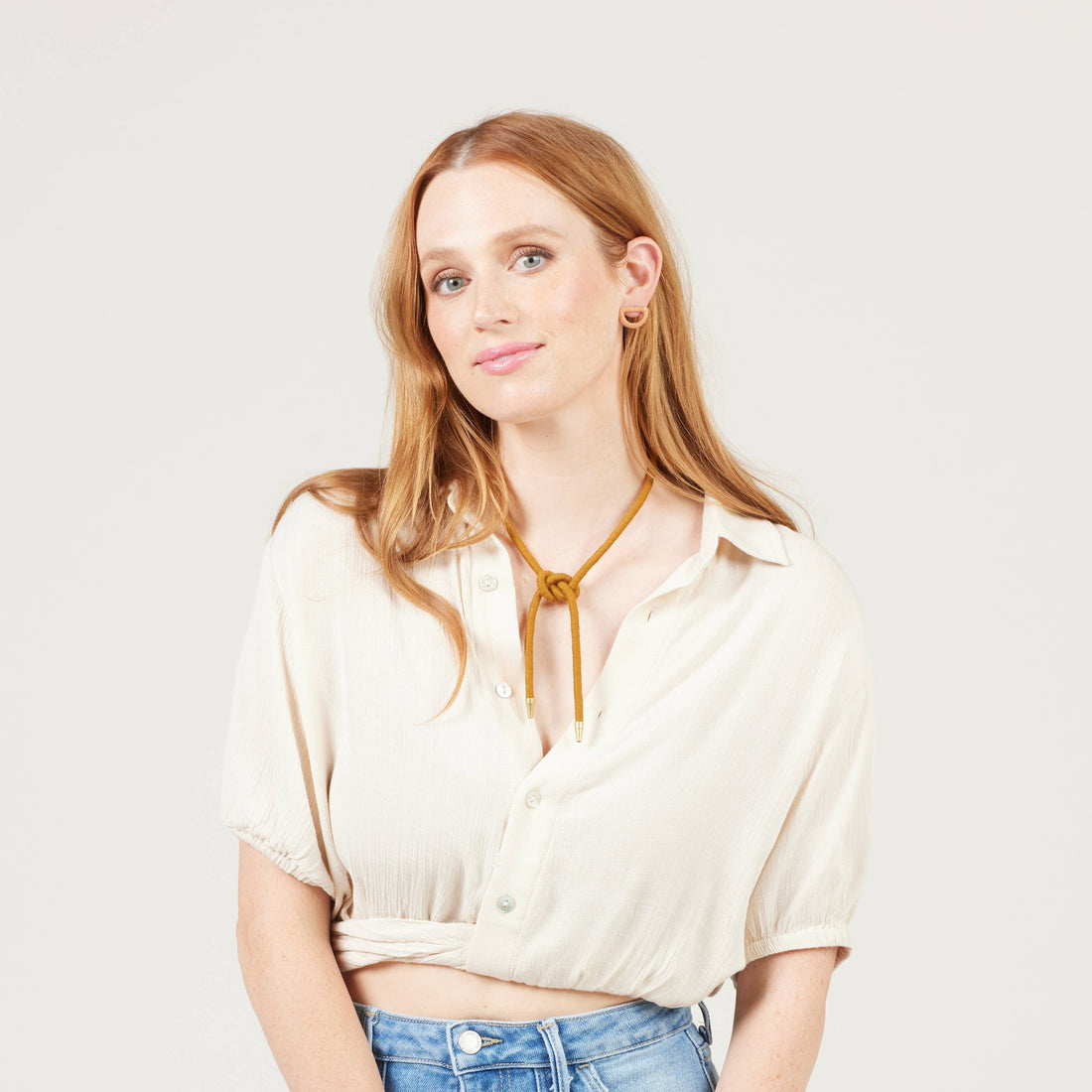 Shoelace Square Knot Bolo tie, golden-ochre cording with raw brass tips, worn on model with knot centered on chest.