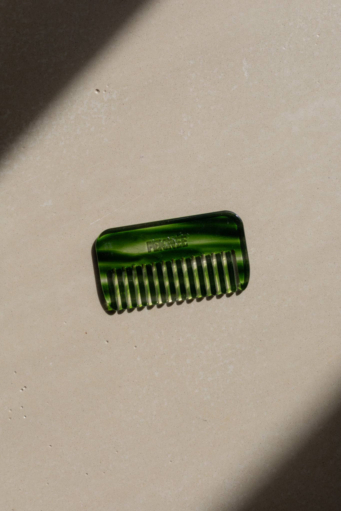 Emerald Travel Wide-Tooth Wave Comb, plant-based cellulose acetate, flat lay on light textured surface with strong diagonal…
