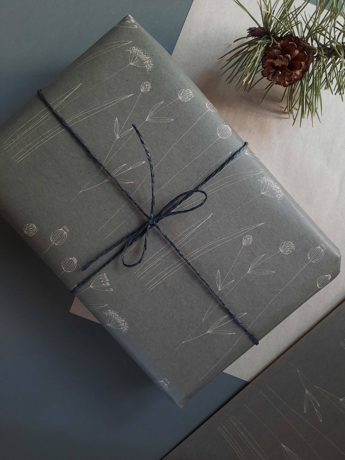 Botanical wrapping paper, dark gray kraft, white illustrated flowers, wrapped gift with dark blue twine and pinecone,…