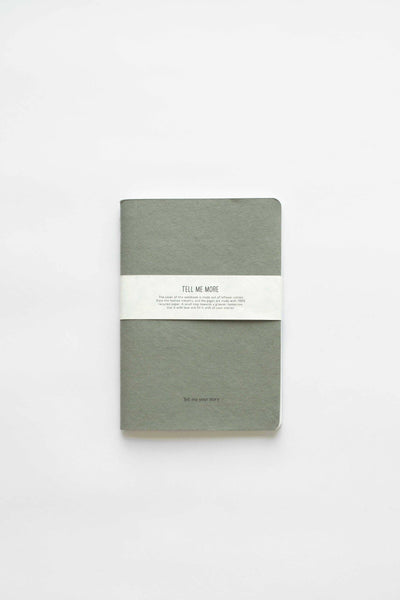 
                    
                      Tell Me More Recycled Paper Notebook, muted sage green recycled cardboard cover, white paper band, flat lay on white.
                    
                  