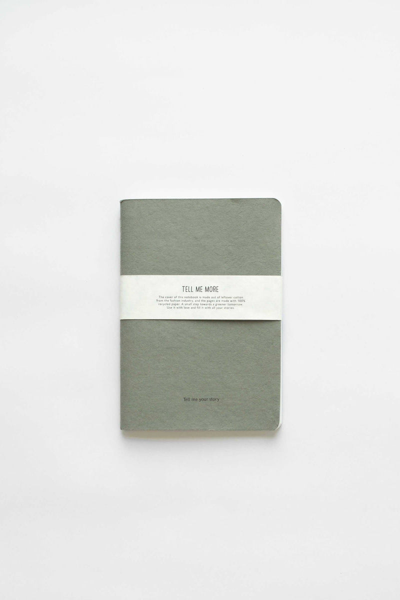 Tell Me More Recycled Paper Notebook, muted sage green recycled cardboard cover, white paper band, flat lay on white.