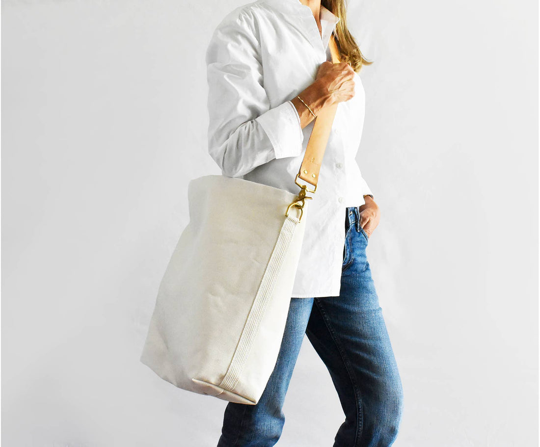 Everyday Tote Bag, natural canvas with tan leather strap & brass hardware, worn on model's shoulder.