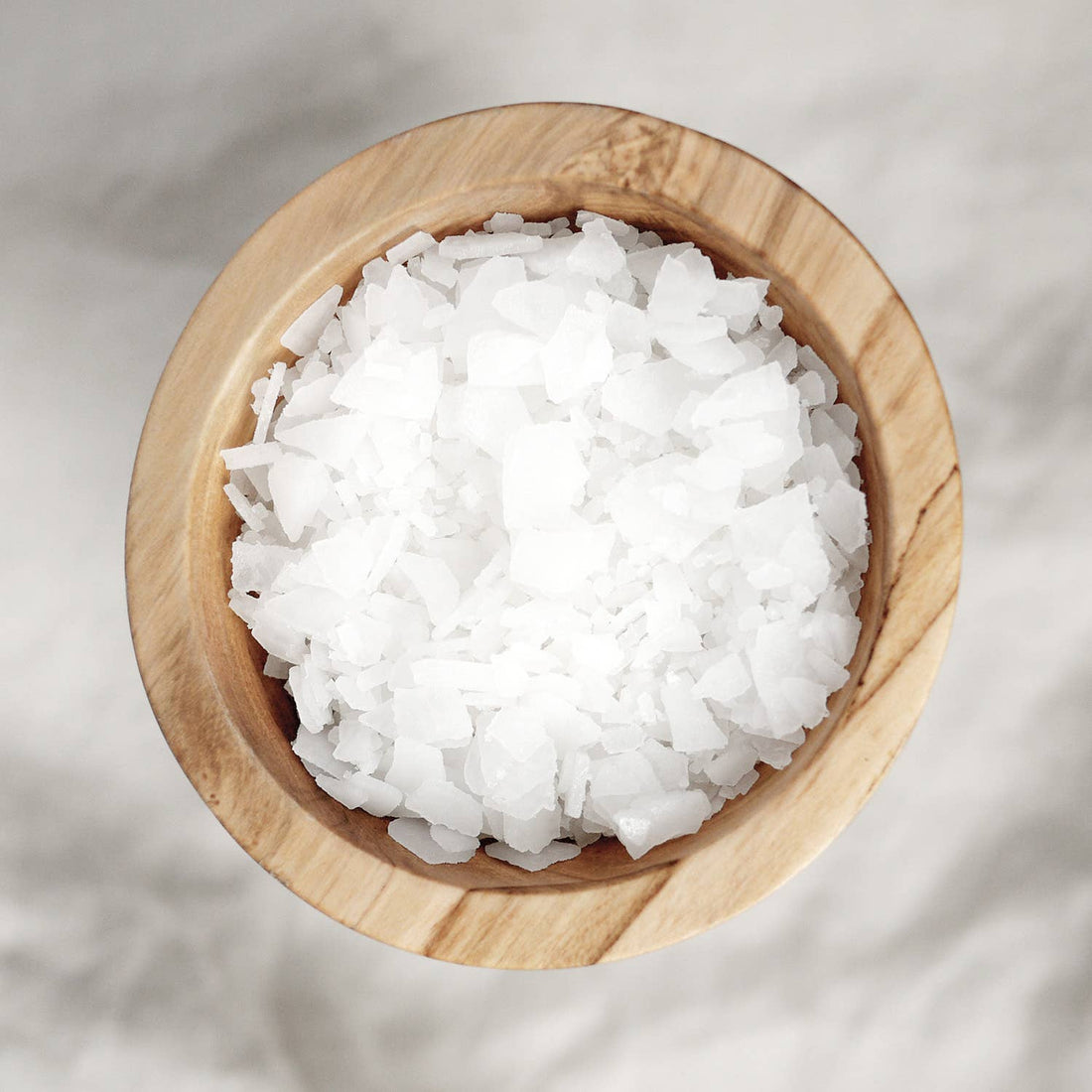 Magnesium Bath Soak, pure magnesium chloride flakes, white jagged crystals in a light wooden bowl, top-down view.