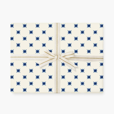 
                    
                      Celebrating Stars wrapping paper, repeating blue star pattern on off-white matte paper, with cream and gold striped ribbon…
                    
                  
