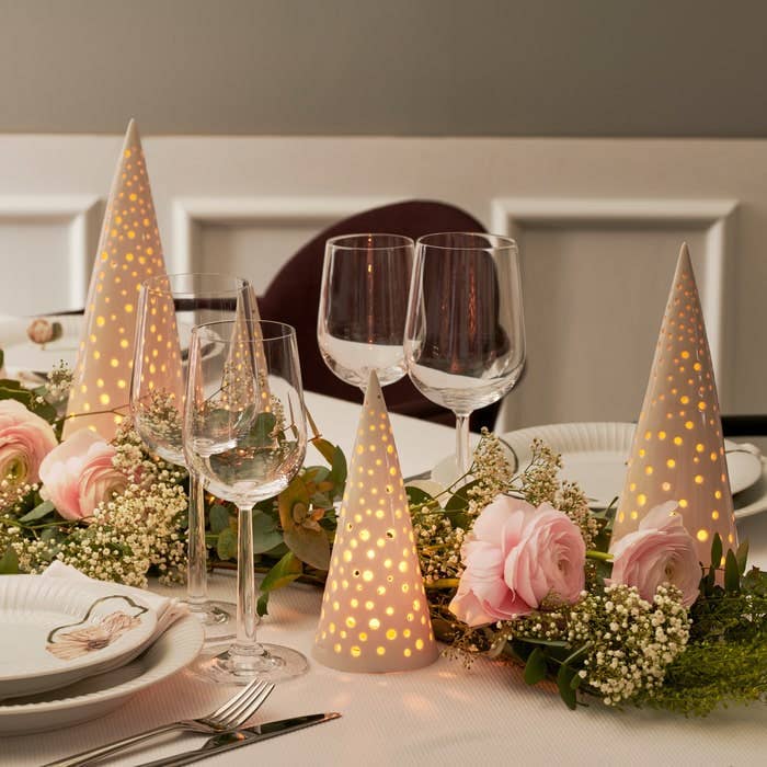 Nobili Ceramic Cone tealight holders, off-white ceramic, glowing dots, grouped on a festive dining table with pink flowers.