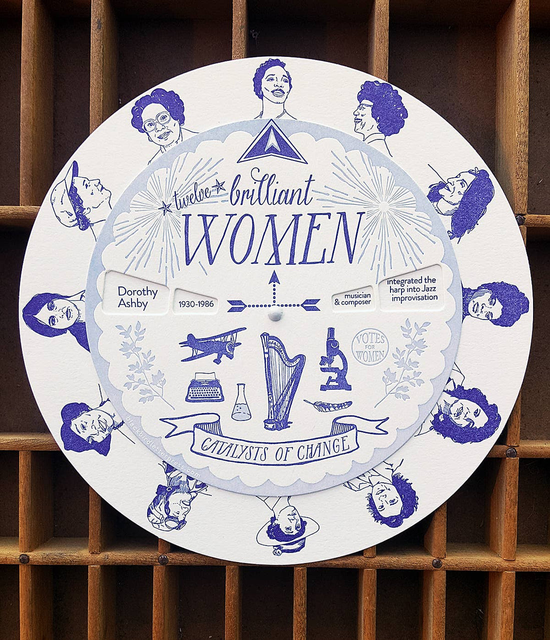 Brilliant Women spinner, white cotton paper, blue illustrations of historical women & accomplishments, angled close-up with…