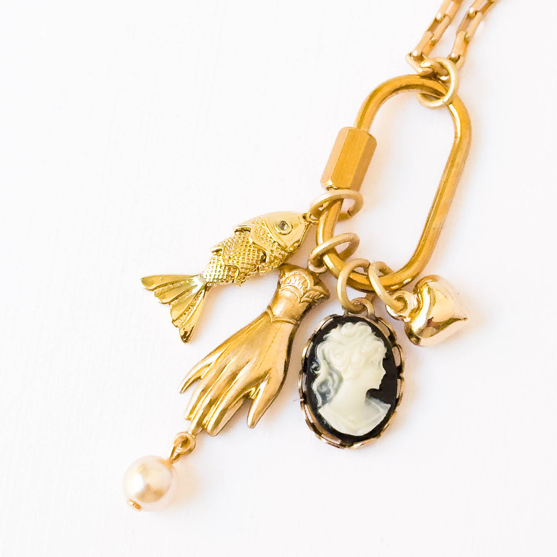 Gold Carabiner Charm Necklace, close-up of 24K gold-plated fish, hand, heart, and black & white cameo charms with a pearl.