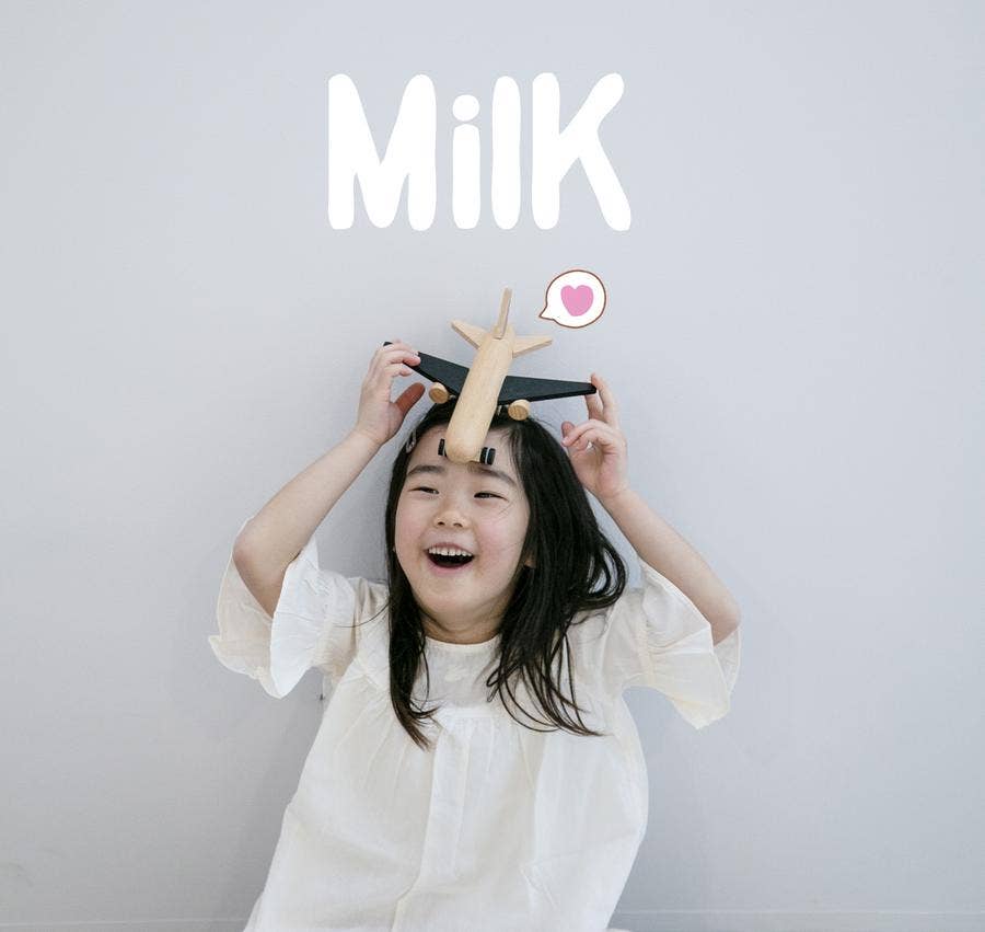 Hikoki Wooden Friction Plane toy, natural beechwood with black wings, held playfully on a smiling child's head for scale.