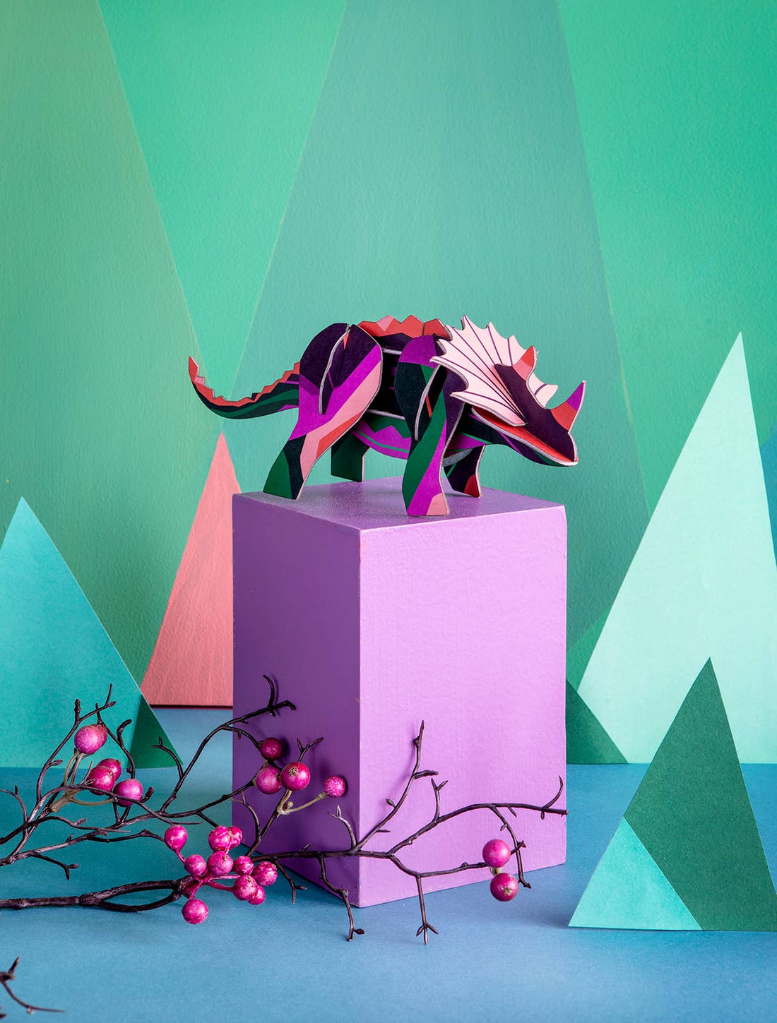 Triceratops 3D model kit, recycled cardboard with vibrant geometric pattern in purple, fuchsia, green, displayed on a purple…