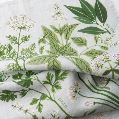 
                    
                      Herb Garden linen tea towel, close-up of folded light blue fabric with green botanical illustrations, including Bay Leaf and…
                    
                  