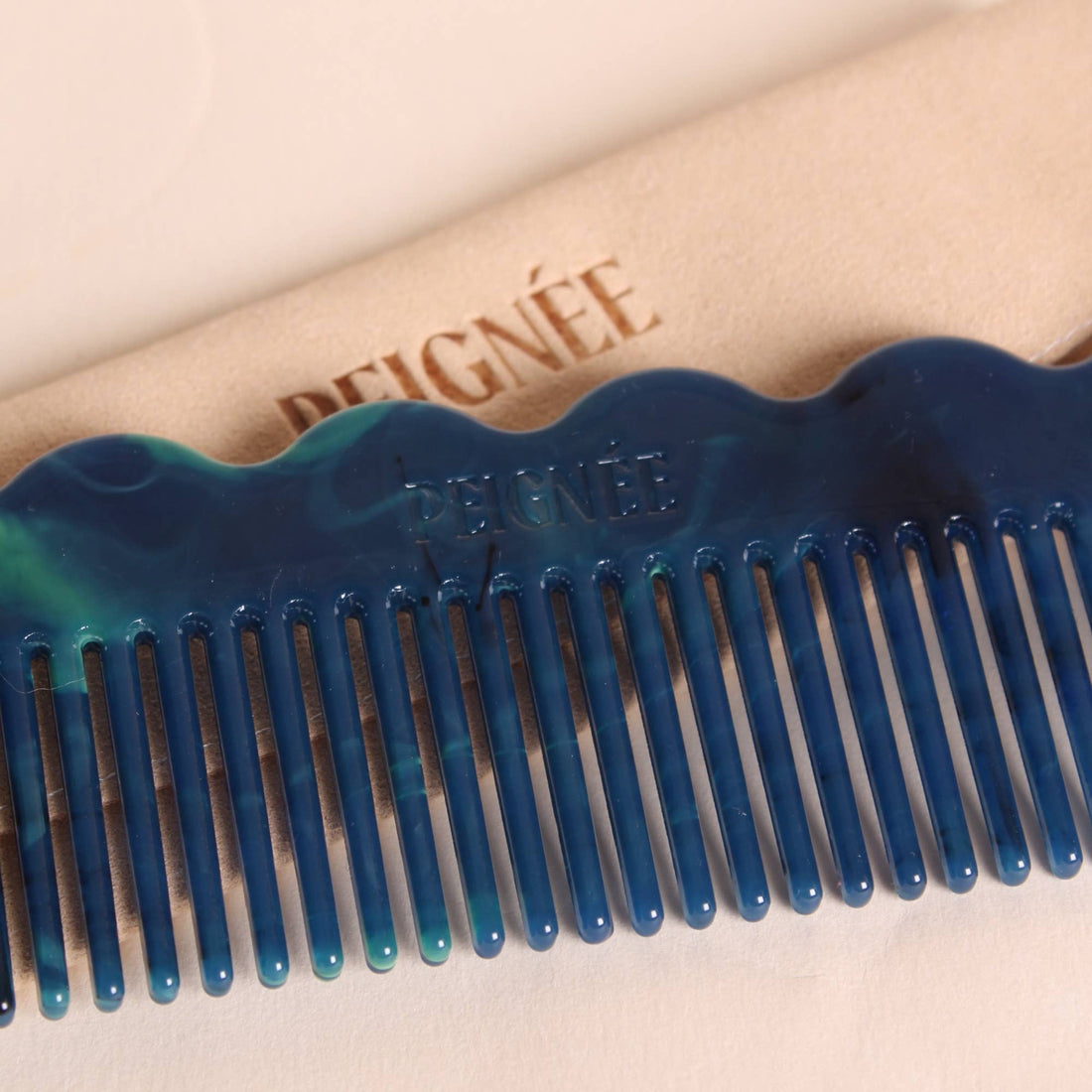 Peignee Signature Wave Comb, deep blue and teal marbled cellulose acetate, close-up of wide teeth, wavy top, and embossed…