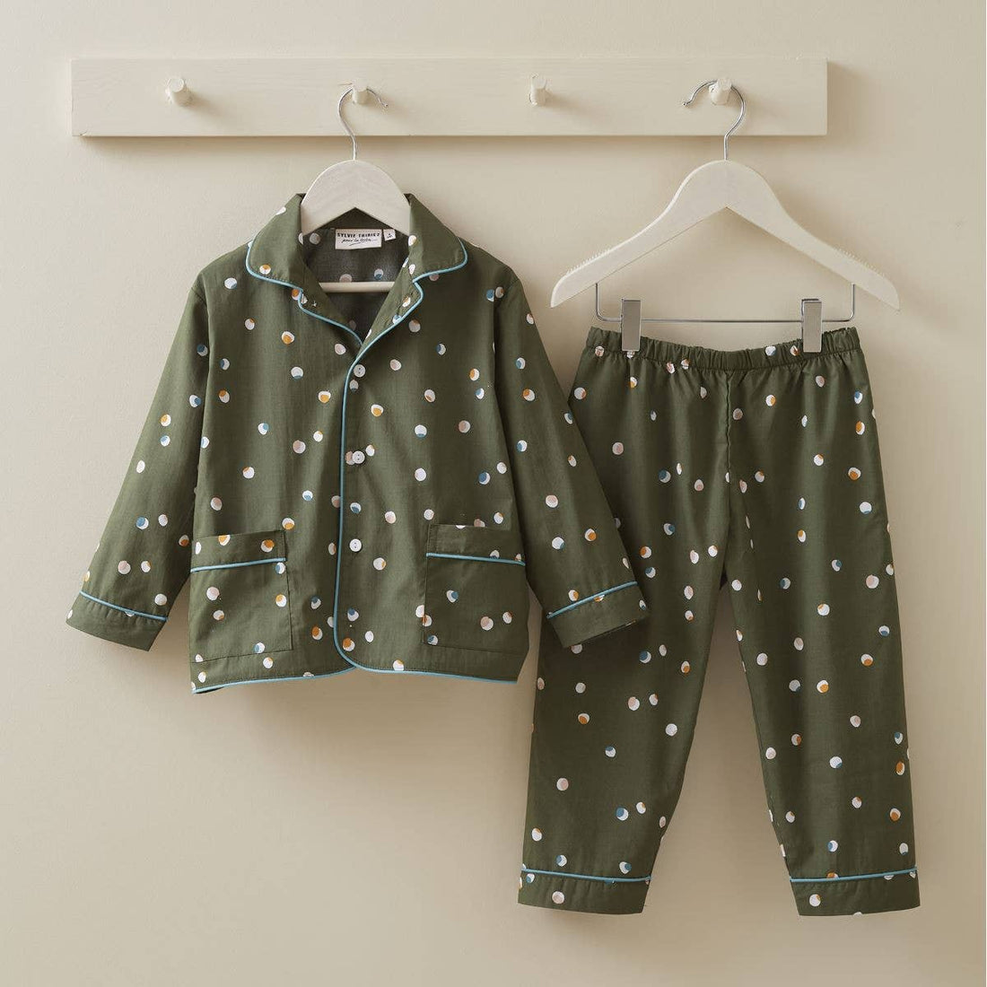Sylvie Thiriez Kids Confetti Pajamas, green cotton with multi-color confetti polka dots and light blue piping, hung on…