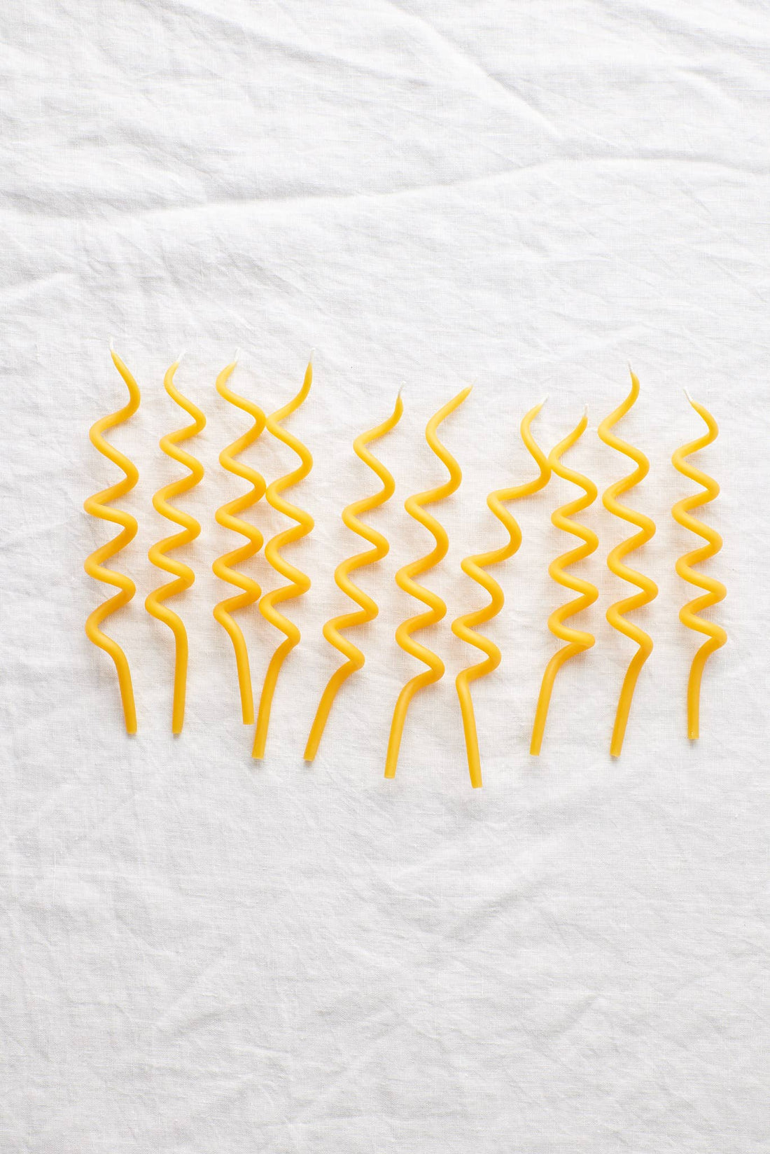 Waxing Moon Twirl Beeswax Birthday Candles, set of eight yellow spiral candles, flat lay on white textured linen.