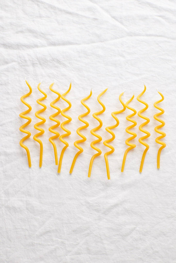 Waxing Moon Twirl Beeswax Birthday Candles, set of eight yellow spiral candles, flat lay on white textured linen.
