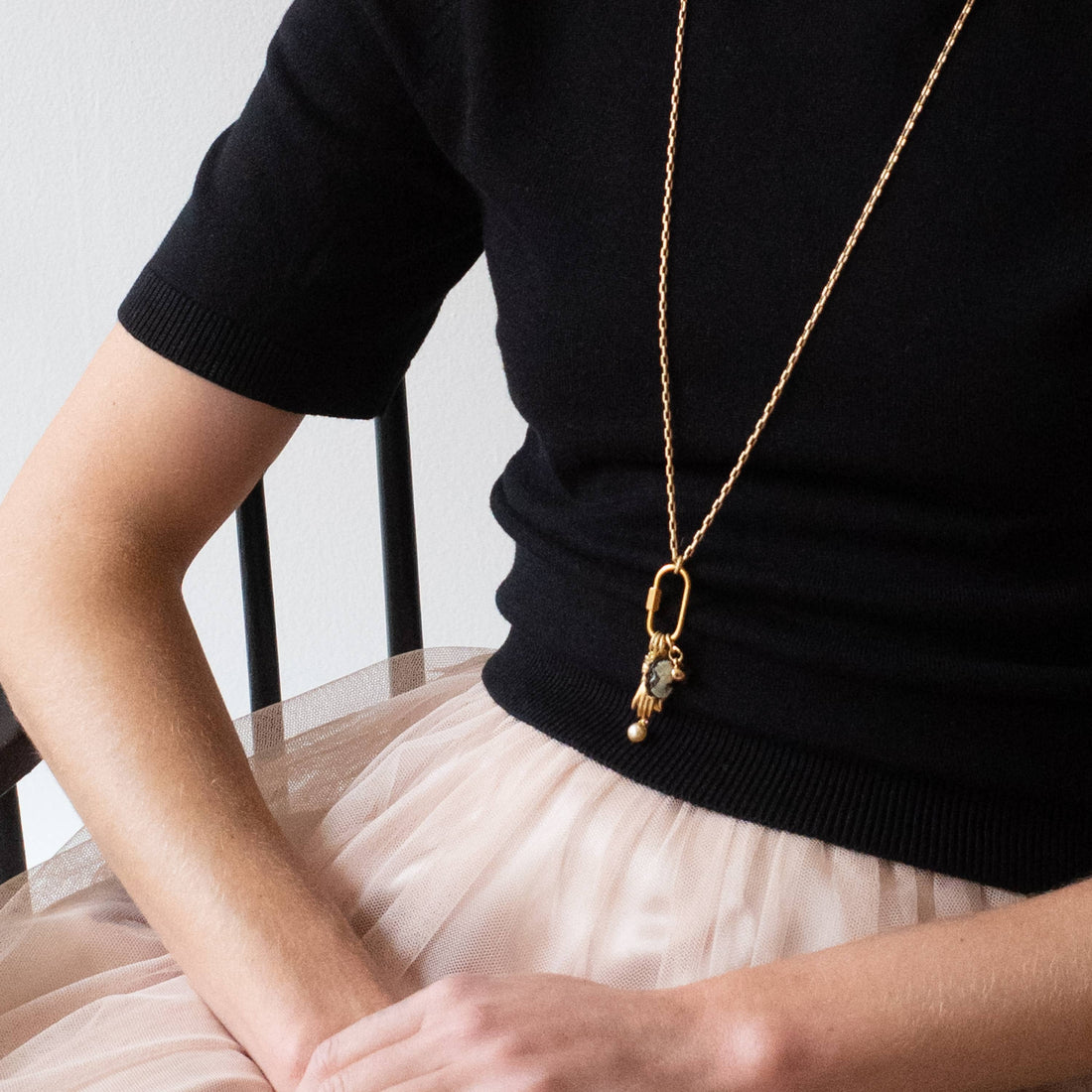 Gold Carabiner Charm Necklace, with cameo, hand, and pearl charms, worn long over a black top.