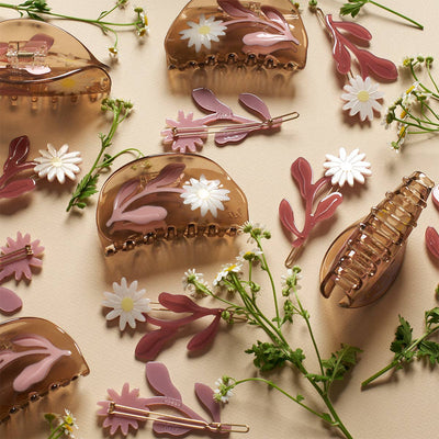 
                    
                      Marguerite Daisy Barrette Set: translucent brown hair claws with white daisies, pink cellulose acetate snap clips, flat lay.
                    
                  