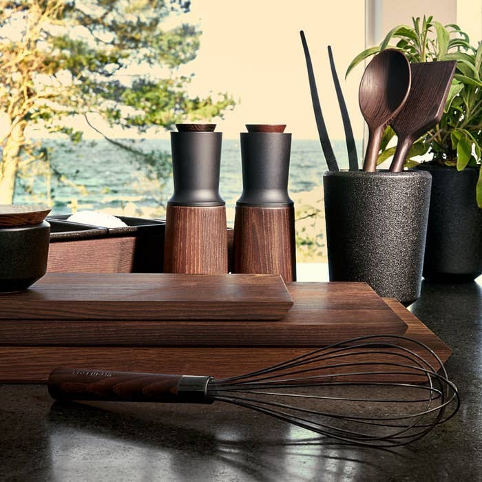 Rå wood cutting boards and serving trays, dark heat-treated ash, neatly stacked on a kitchen counter.