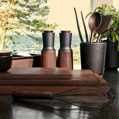 
                    
                      Rå wood cutting boards and serving trays, dark heat-treated ash, neatly stacked on a kitchen counter.
                    
                  