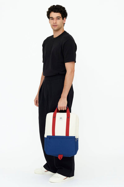 
                    
                      Daily 15" Bauhaus Block backpack in creamy white, royal blue, and red Oxford RPET fabric, held by a man for scale.
                    
                  