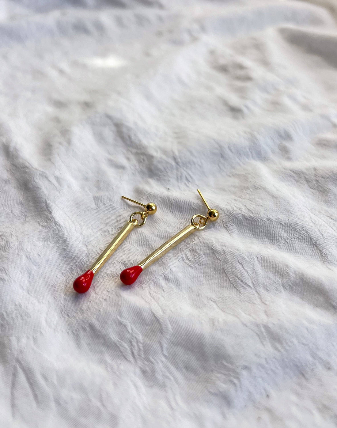 Matchstick earrings, 18k gold plated with red tips, flat lay pair showing gold ball stud backings.