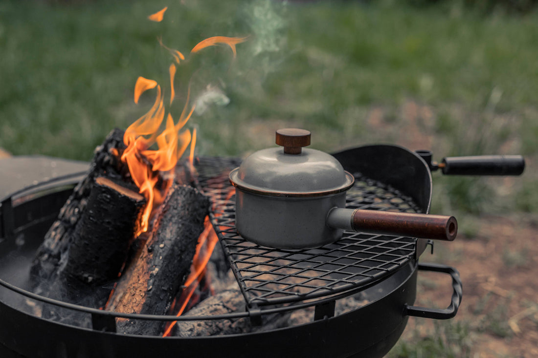 Enamel Saucepan with Walnut Handle, grey speckled enamel, steaming on a charcoal grill over burning logs.