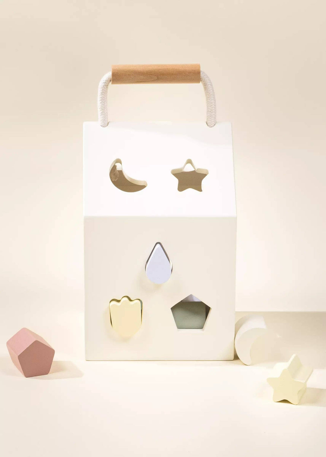 White wood Shapes Sorting House with natural wood handle, showing star, moon cutouts, and pastel geometric blocks.
