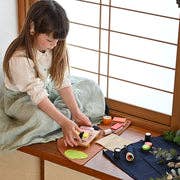 Child playing with Sushi Party Set wooden play food, arranging beechwood sushi on a denim mat on a window sill.