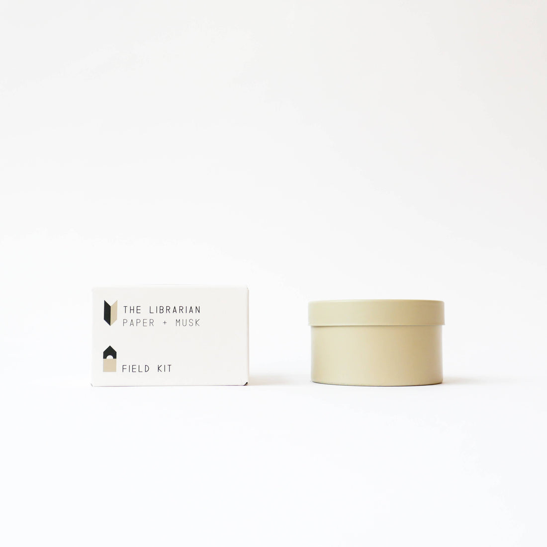 Field Kit The Librarian tin candle, Paper + Musk scent. Light beige tin next to white packaging box, front view on white.
