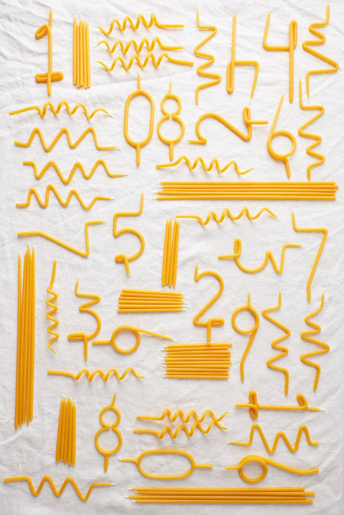 Traditional Birthday Candles, pure yellow beeswax, flat lay showcasing a large assortment of straight, wavy, and…