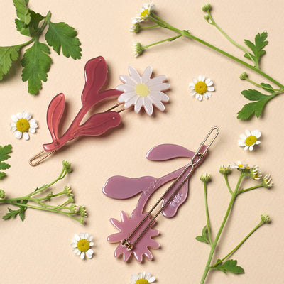 
                    
                      Daisy Barrette Set, translucent reddish-pink leaf with white flower, purple leaf with flower shown from back revealing gold…
                    
                  