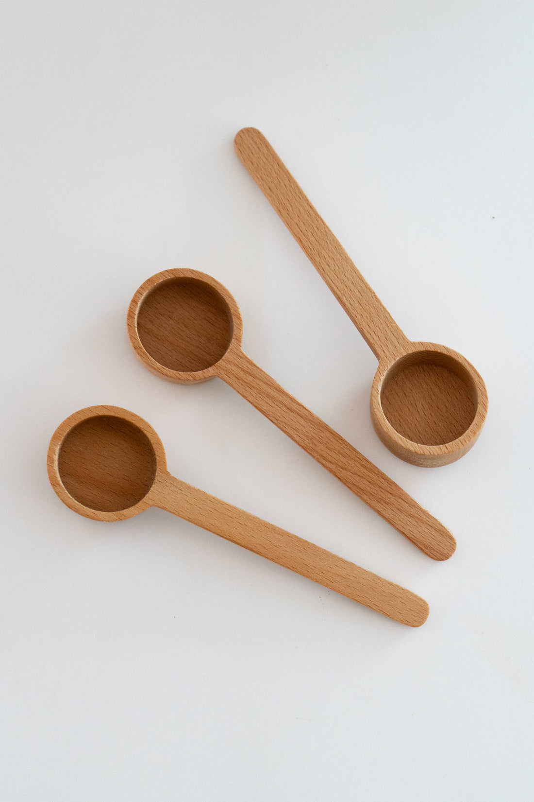 Three Wooden Tea Scoops made of unfinished beechwood, shown in a staggered overhead flat lay.