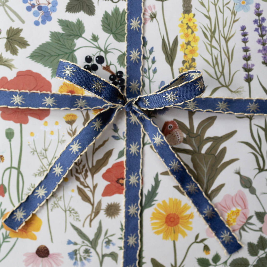Stars Embroidered Ribbon, dark blue with gold stars and scalloped edge, tied in a bow on botanical gift wrap.