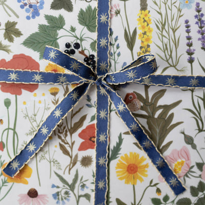 
                    
                      Stars Embroidered Ribbon, dark blue with gold stars and scalloped edge, tied in a bow on botanical gift wrap.
                    
                  