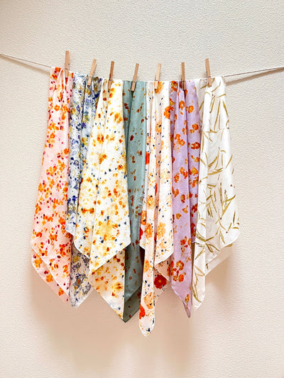 
                    
                      Naturally dyed silk bandana scarves, like Abby's blossom patterns, displaying varied hues hanging on a clothesline.
                    
                  