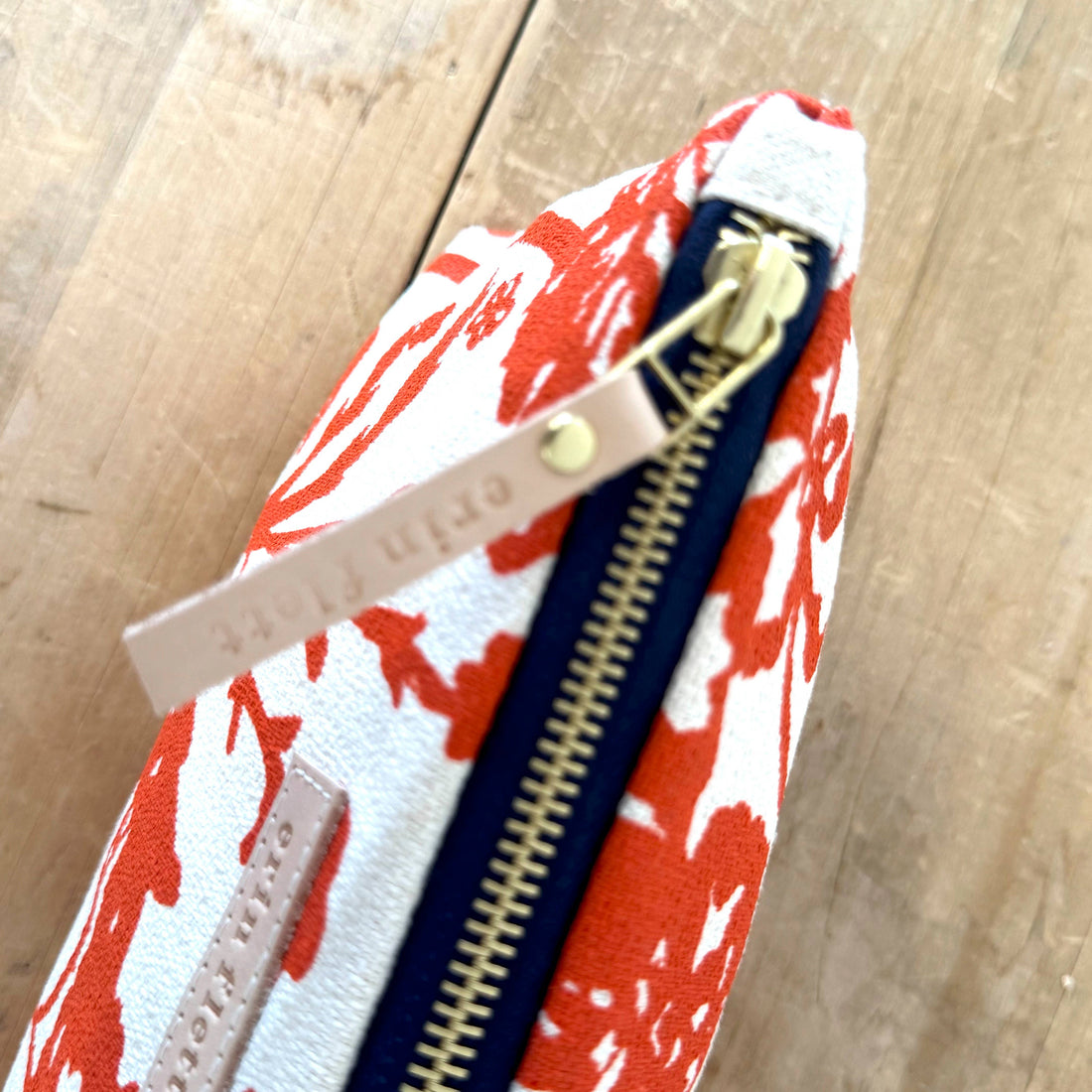 Erin Flett Laura cosmetic pouch, Flaggy Meadow pattern close-up. Features brass zipper, navy tape, and embossed leather pull.