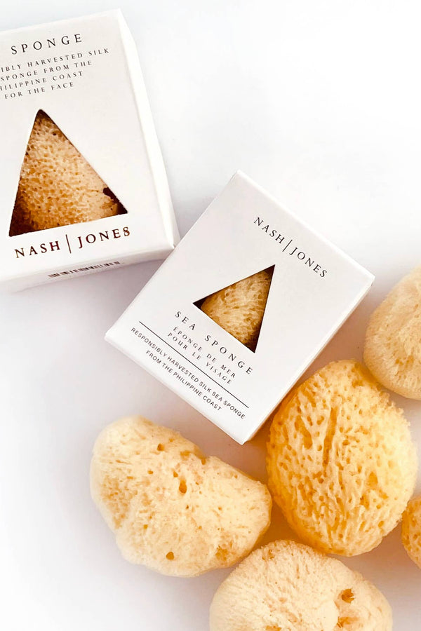Nash and Jones Sea Sponge, natural tan silk exfoliation sponges in white boxes and several loose, porous sponges, flat lay…