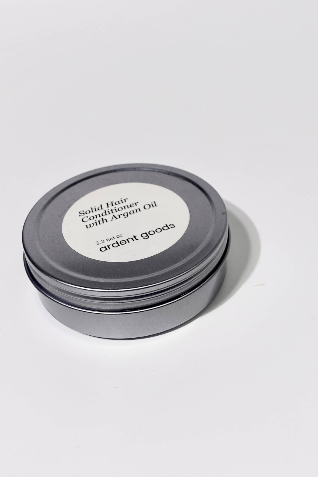 Solid Hair Conditioner with Argan Oil in a round silver tin with white label, angled view showing top and side.