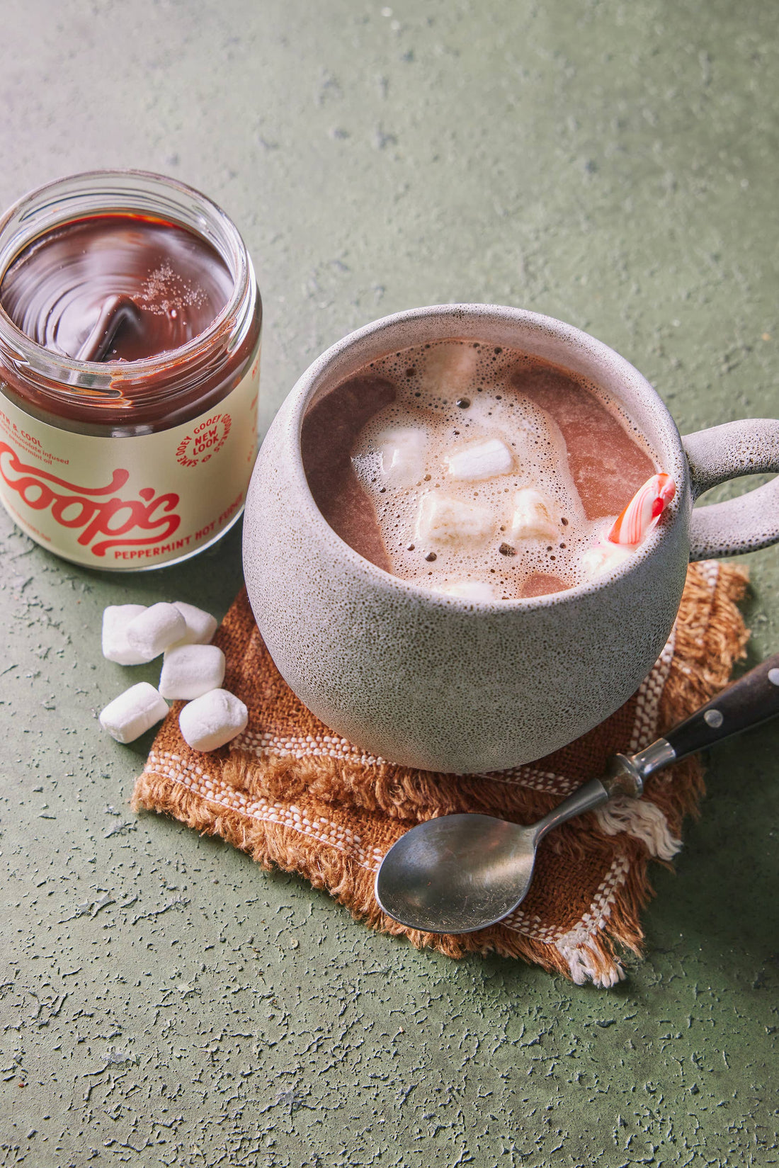 Peppermint Hot Fudge sauce in open glass jar, showing dark chocolate, paired with hot chocolate, melting marshmallows, and…