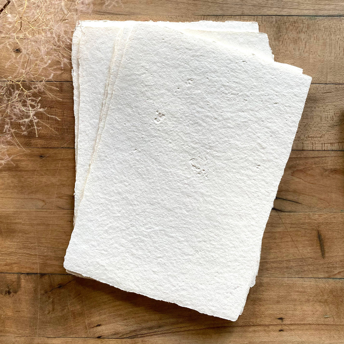 Ivory Handmade Paper Set, stack of thick recycled cotton sheets, close-up showcasing rough, fibrous texture and torn deckled…