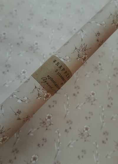 
                    
                      Vintage Blooms wrapping paper roll, light beige with delicate floral pattern, close-up of brown paper band detail showing…
                    
                  