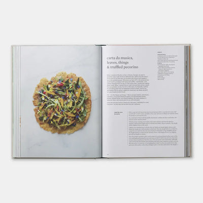 
                    
                      On Vegetables cookbook open to 'carta da musica' recipe, crisp bread with vegetables and flowers.
                    
                  